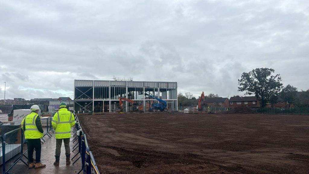 School building under construction at Shottery, with site staff and construction machinery in the foreground